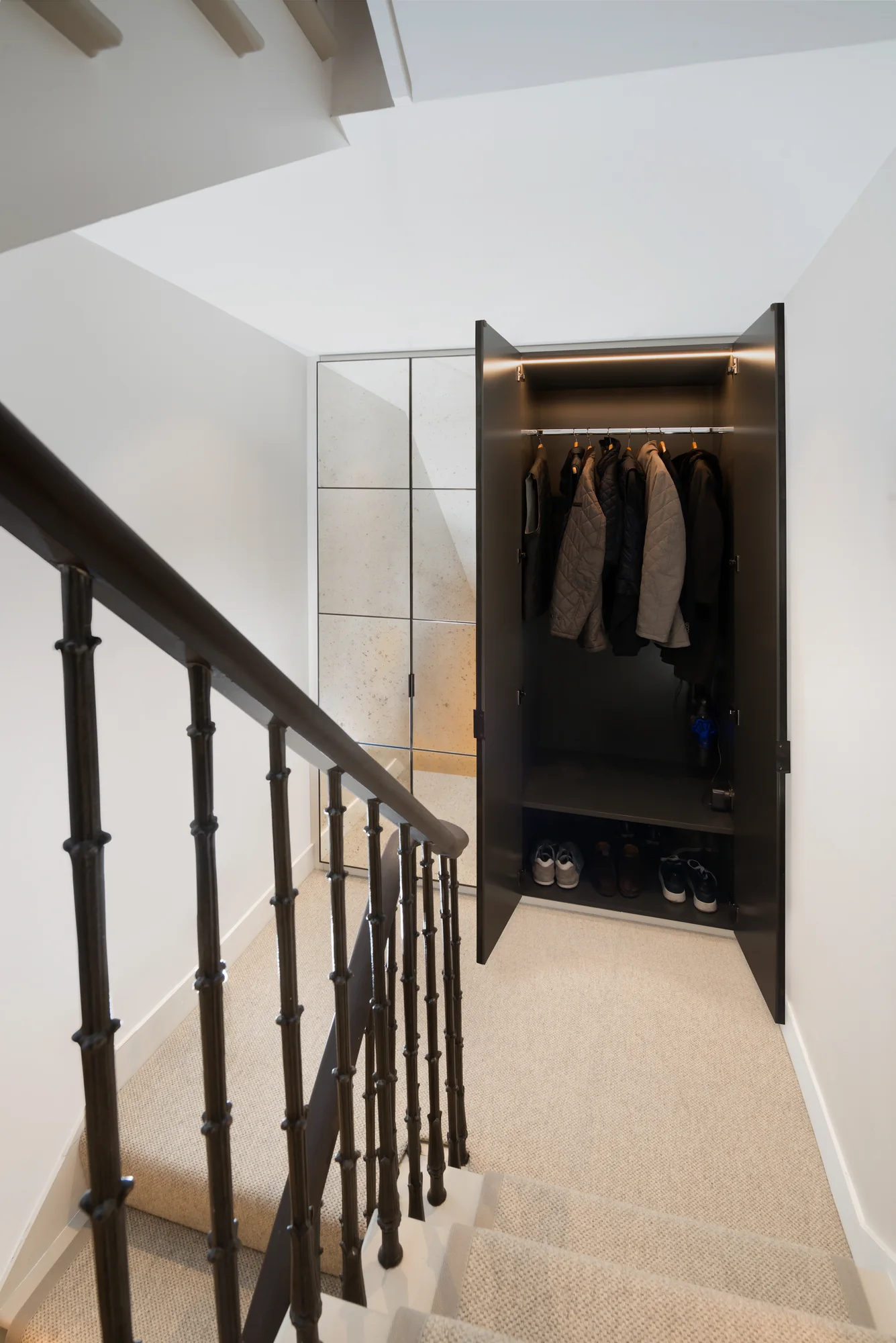 Open mirrored hallway wardrobe revealing hanging coats, an upper shelf and shoe storage
