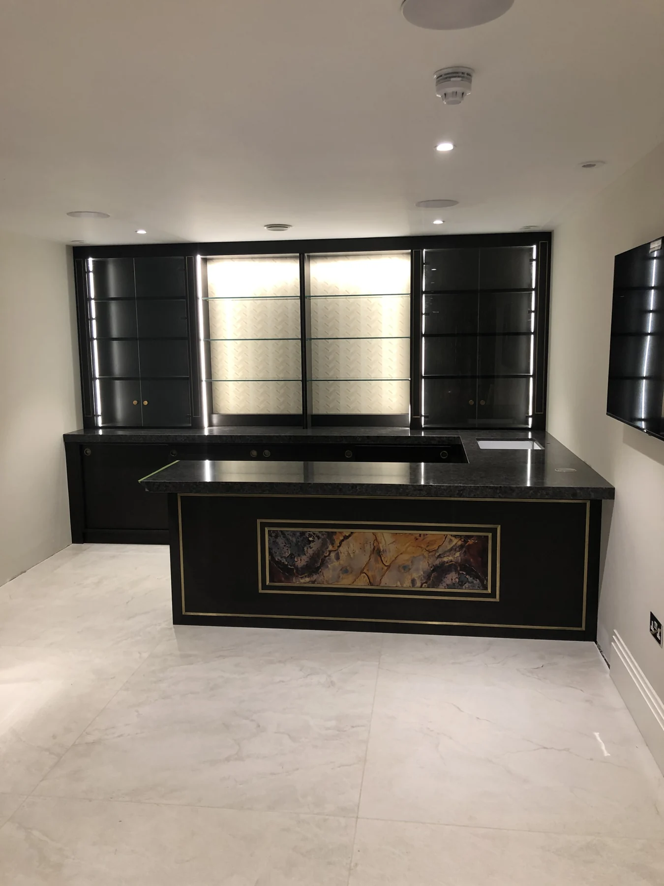 Black bar island with a decorative front panel and illuminated display cabinetry.
