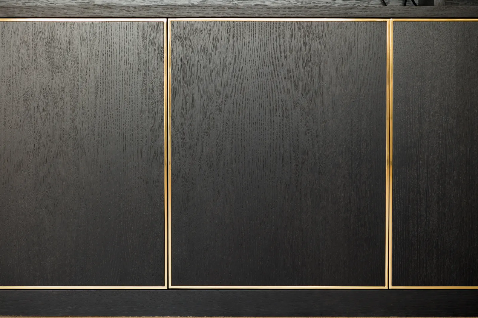 Close-up of black oak grain and brass-toned inlay on media cabinet fronts