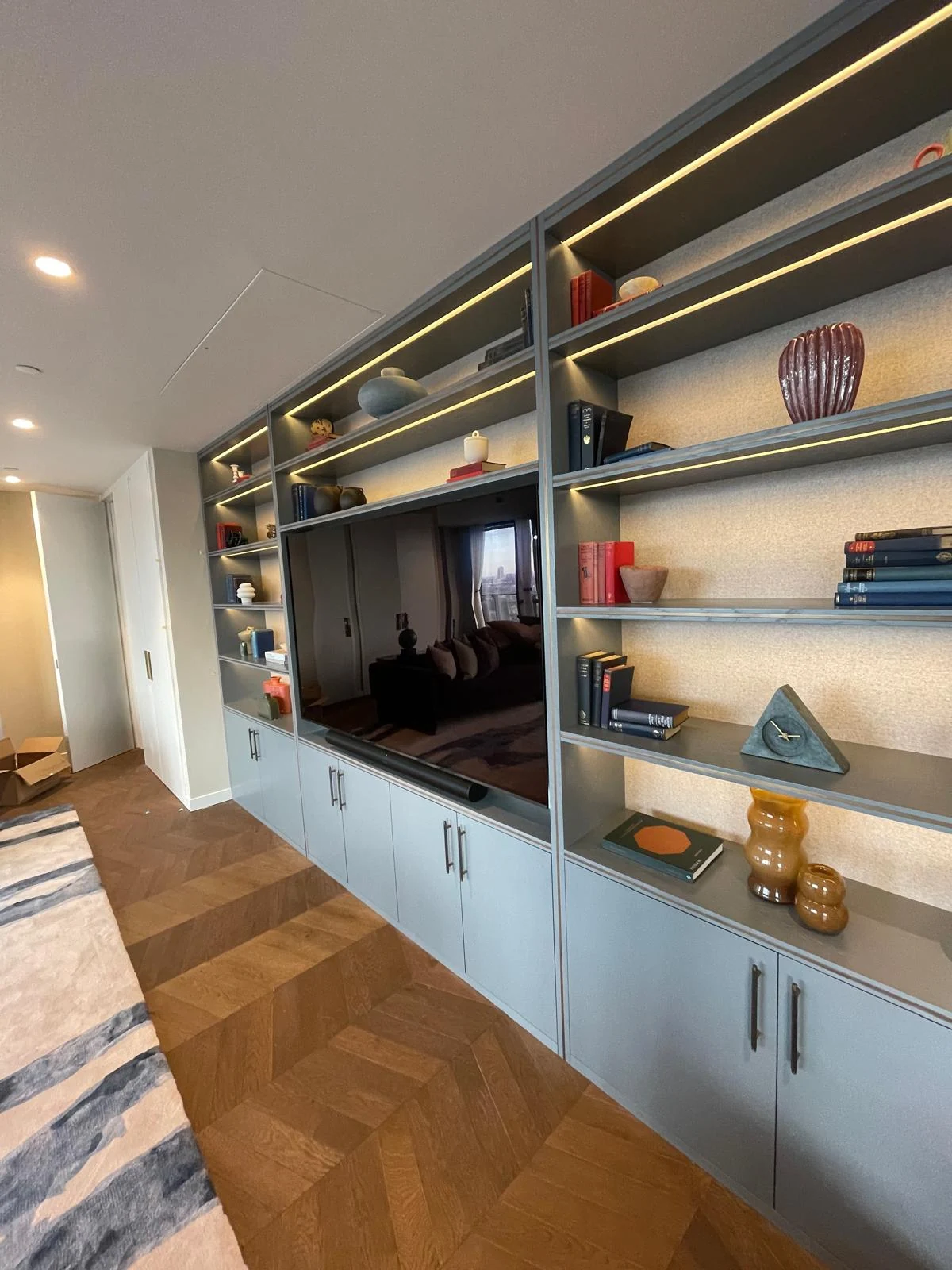 Side view along blue-grey lower cupboards and illuminated open shelves.