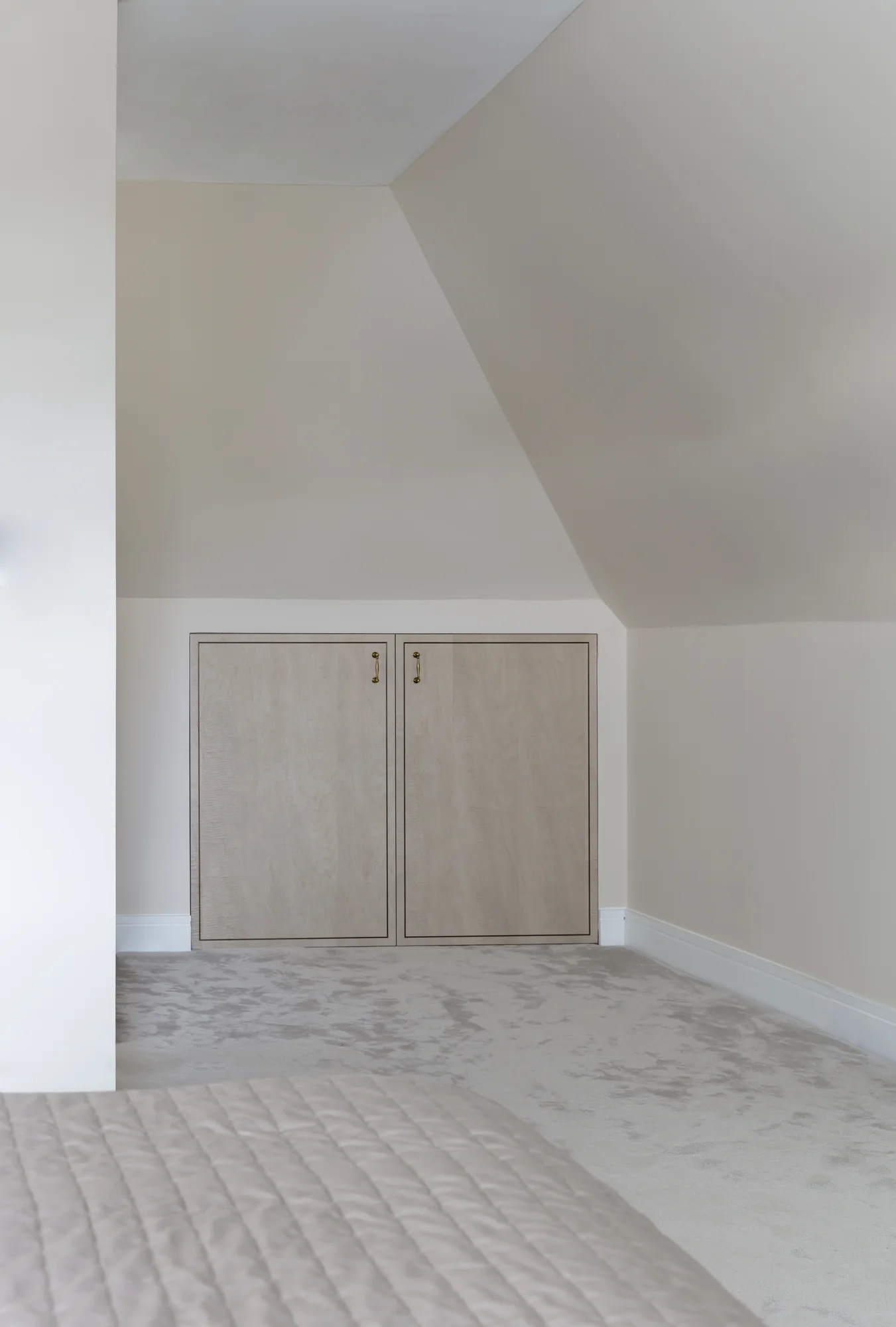 Pale two-door fitted cupboard in the low wall beneath a sloping ceiling