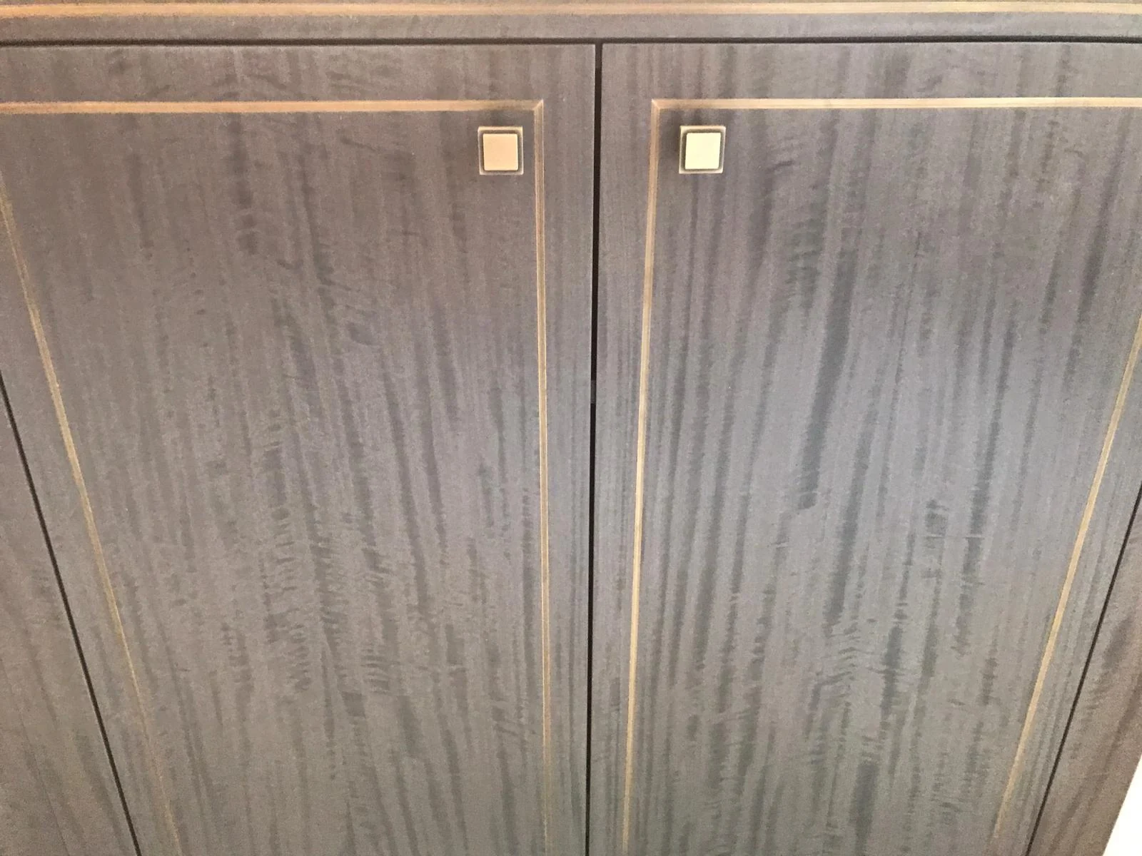 Dark wood-grain cabinet doors with fine metallic-tone outline details and square pulls.