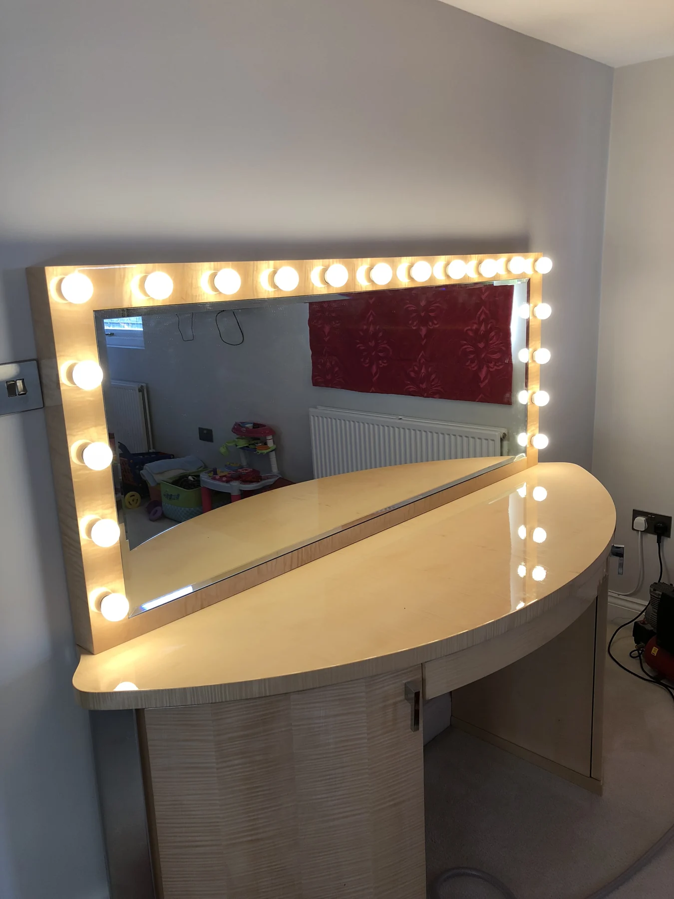 Curved dressing table with built-in storage and a bulb-framed mirror.