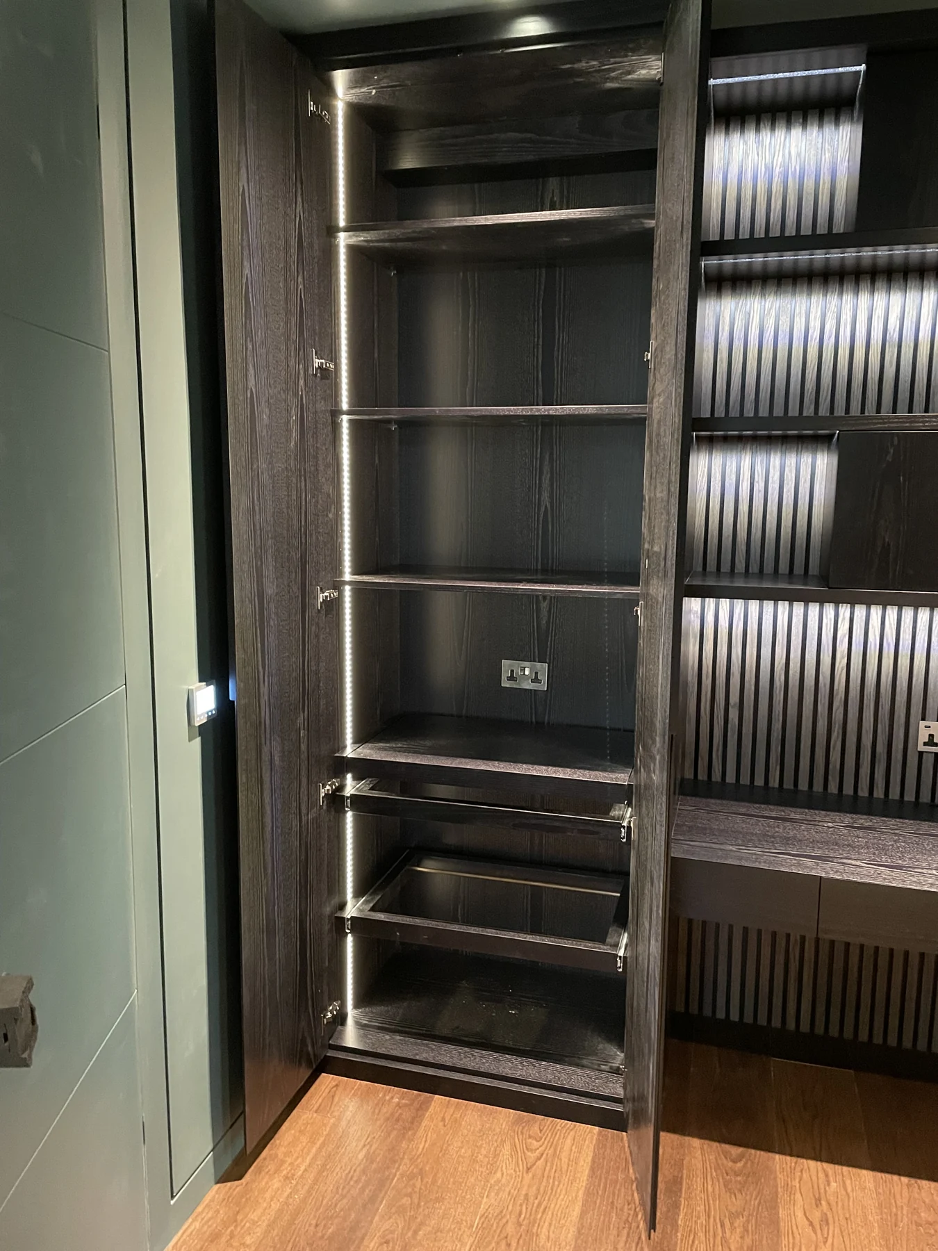 Open tall cupboard beside the dark illuminated shelving and low storage.