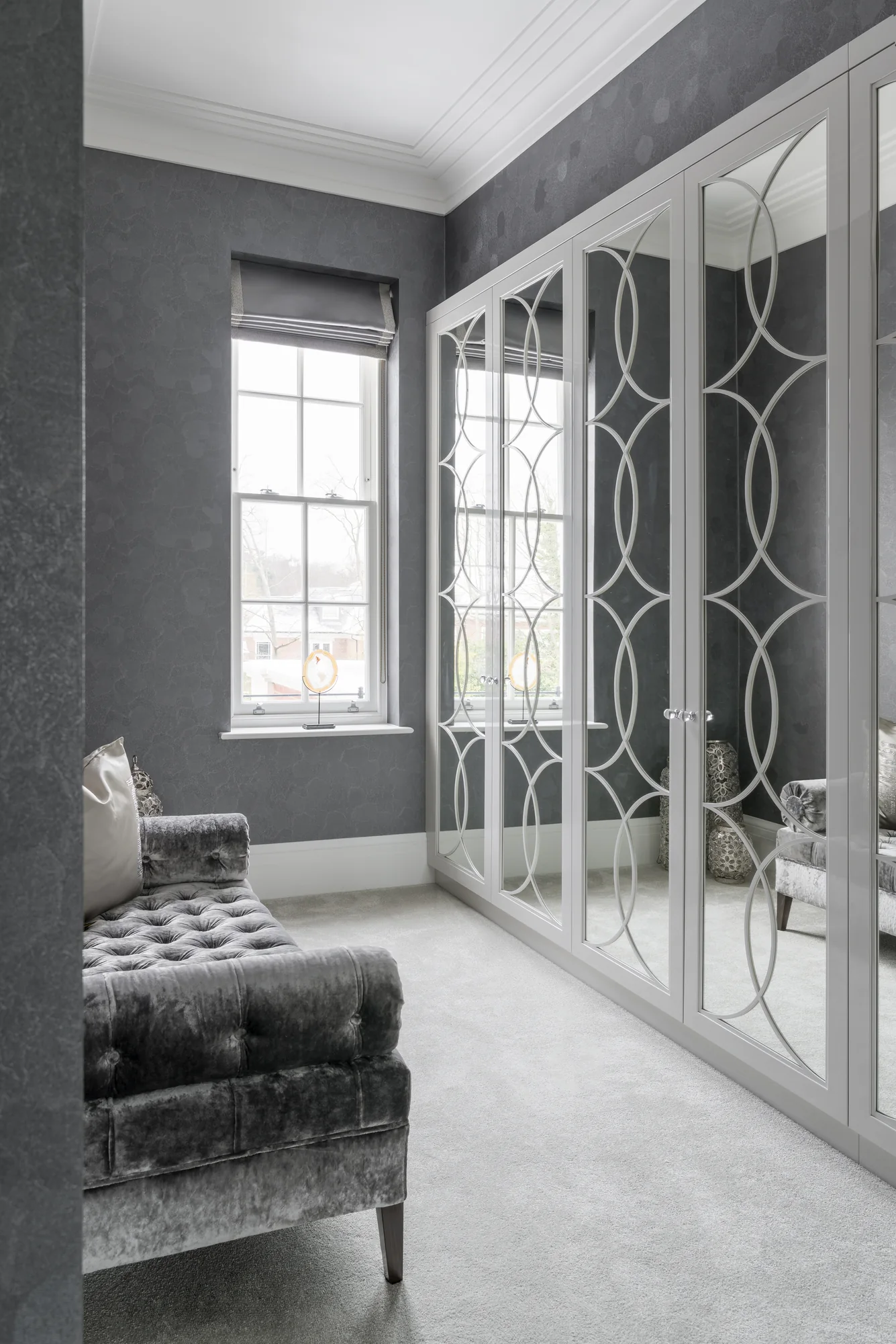 Closed mirrored wardrobe doors with pale circular patterns beside a window