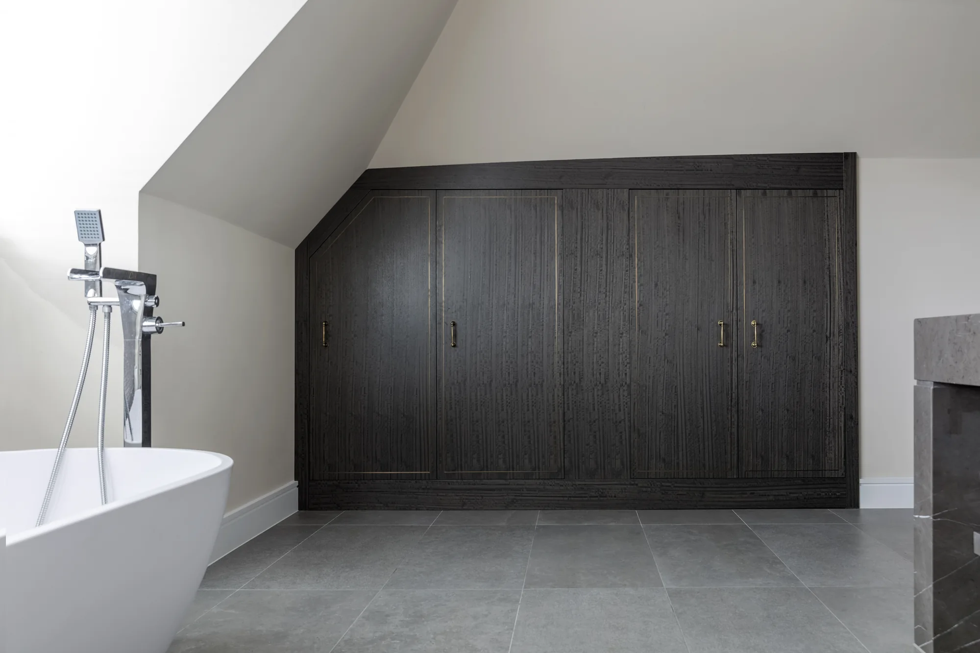Dark bathroom cupboards with closed doors shaped beneath a sloping ceiling