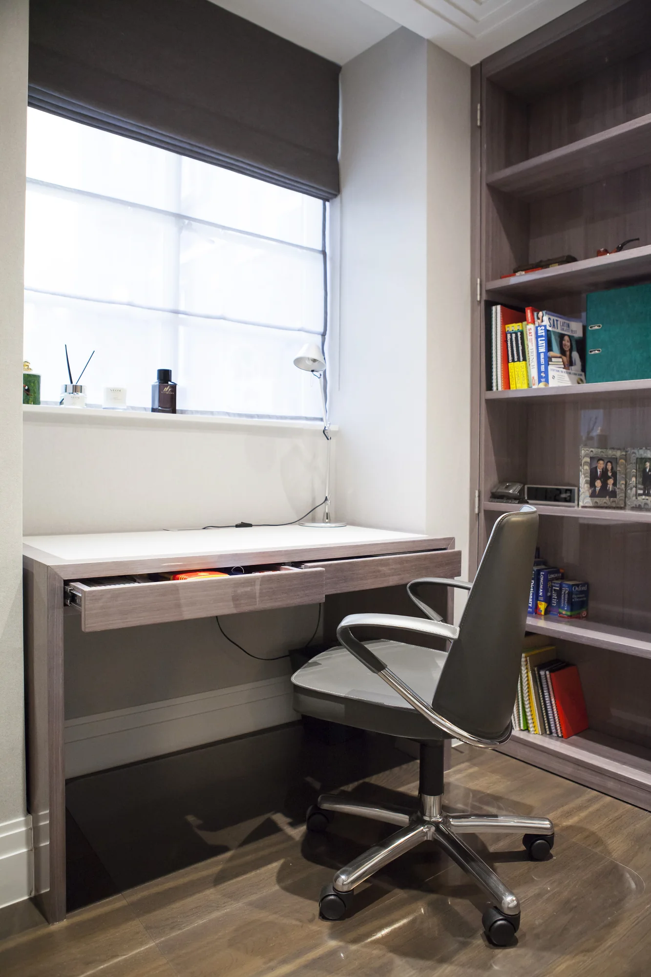 Fitted bedroom desk beneath a window beside a tall bookcase, with its drawer open