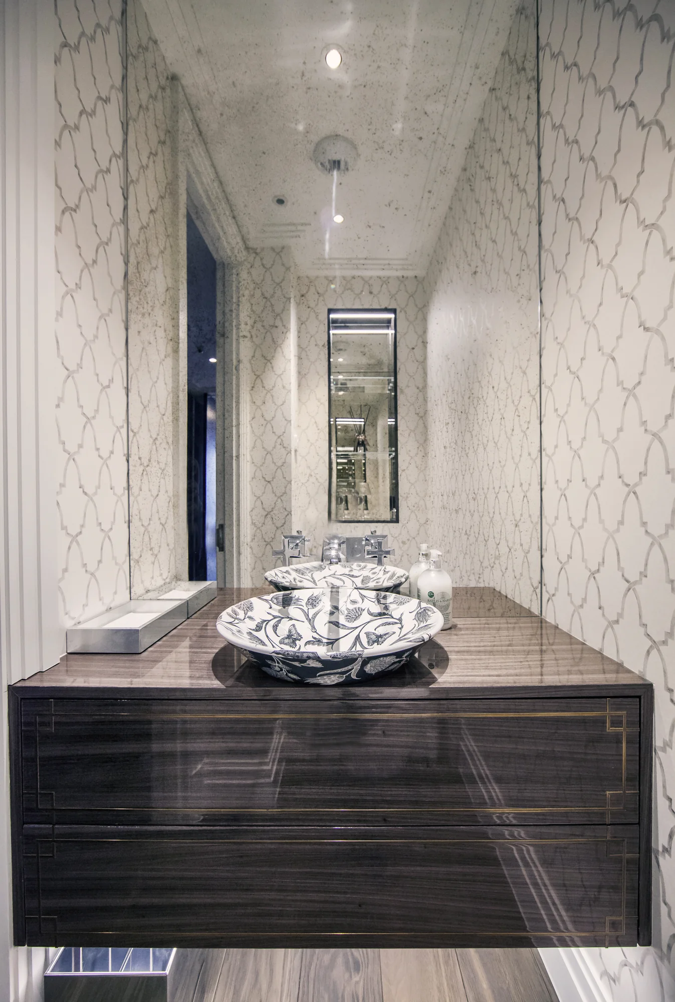 Dark floating cloakroom vanity beneath a decorative bowl basin and patterned wall