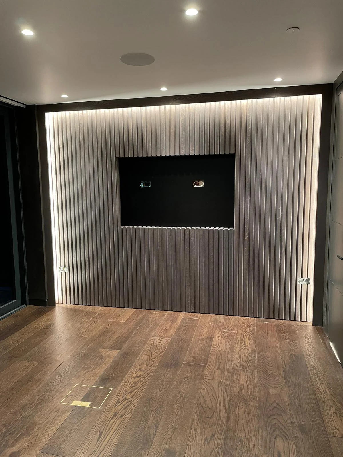 Vertically fluted television feature wall with a continuous upper lighting strip.