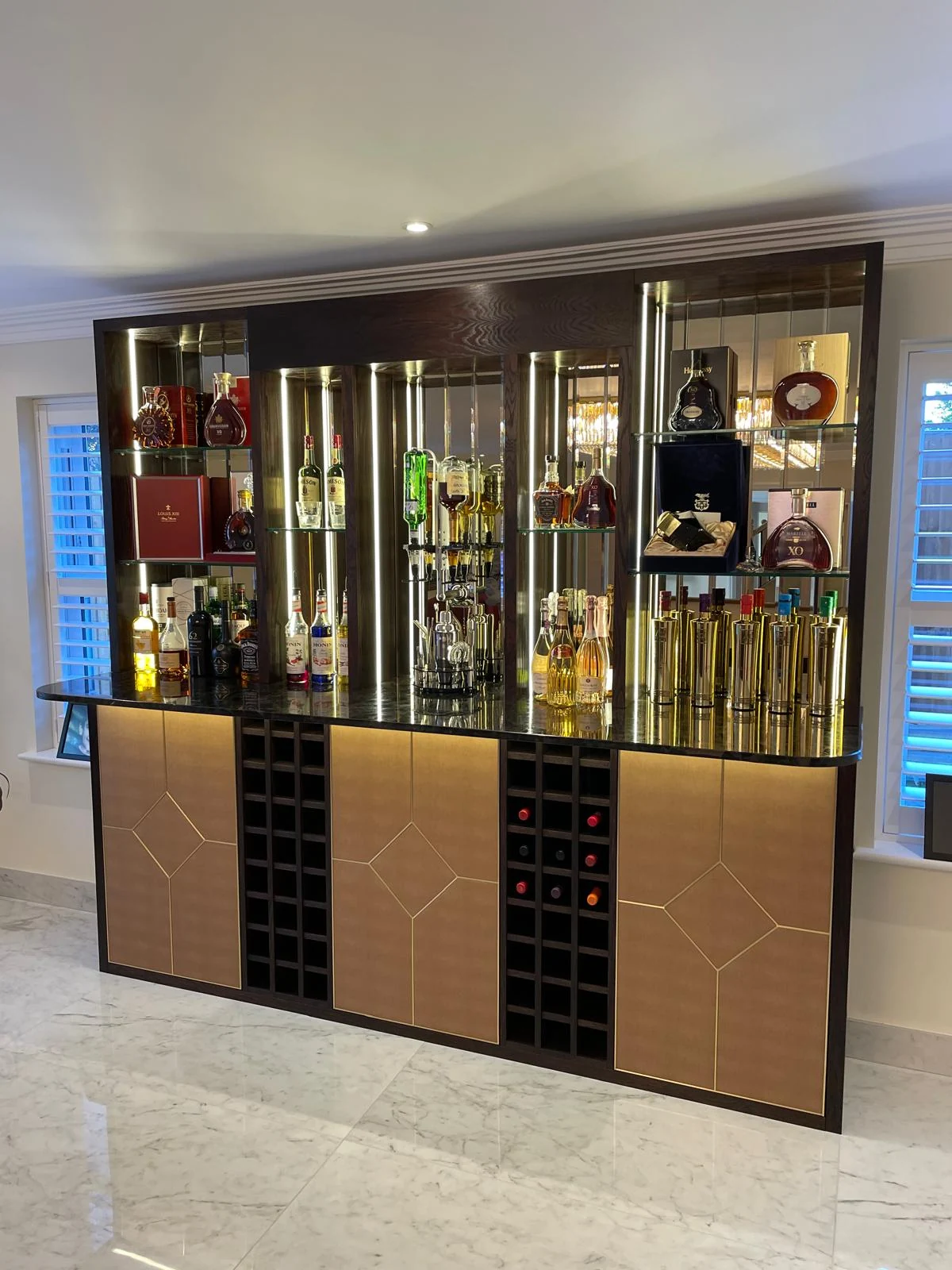 Wide view of the mirrored drinks cabinet, gold-tone doors and wine storage.