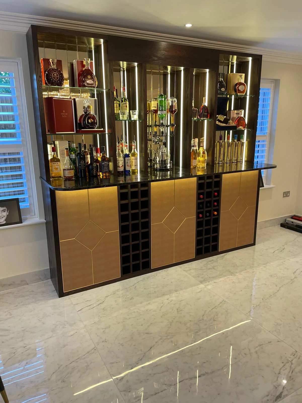 Mirrored drinks cabinet with gold-tone lower doors and bottle-storage grids.