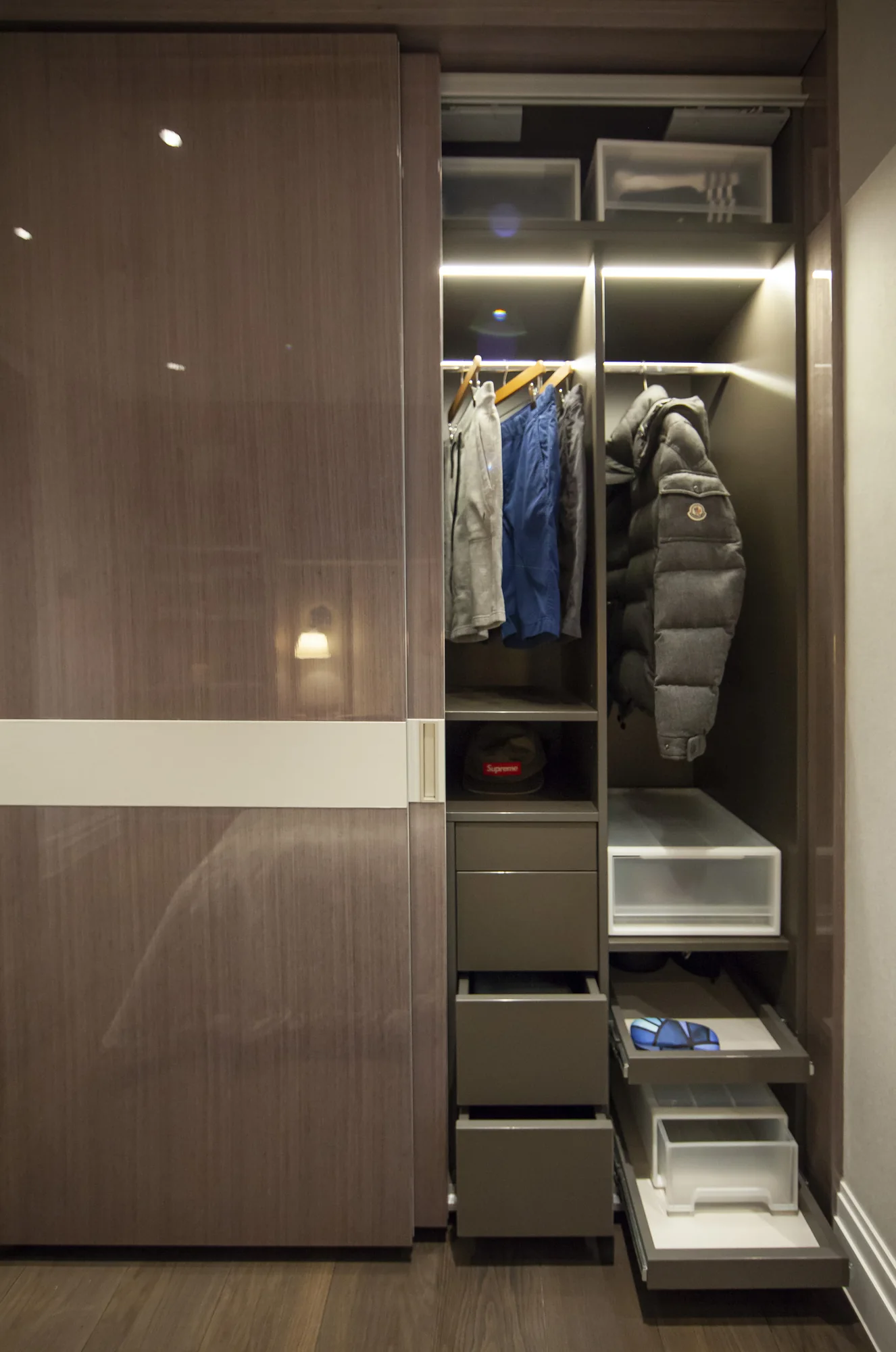 Illuminated wardrobe interior with hanging clothes and pull-out storage