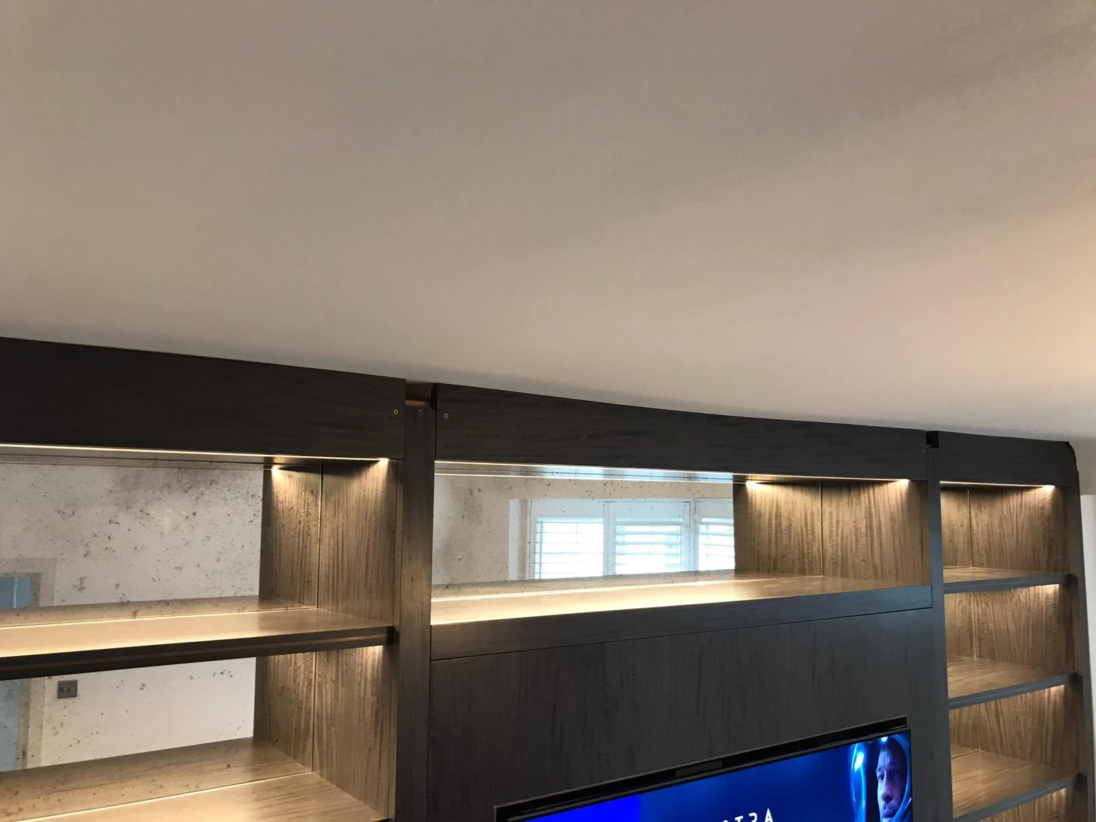 Close view of upper display shelves and concealed lighting above the television.