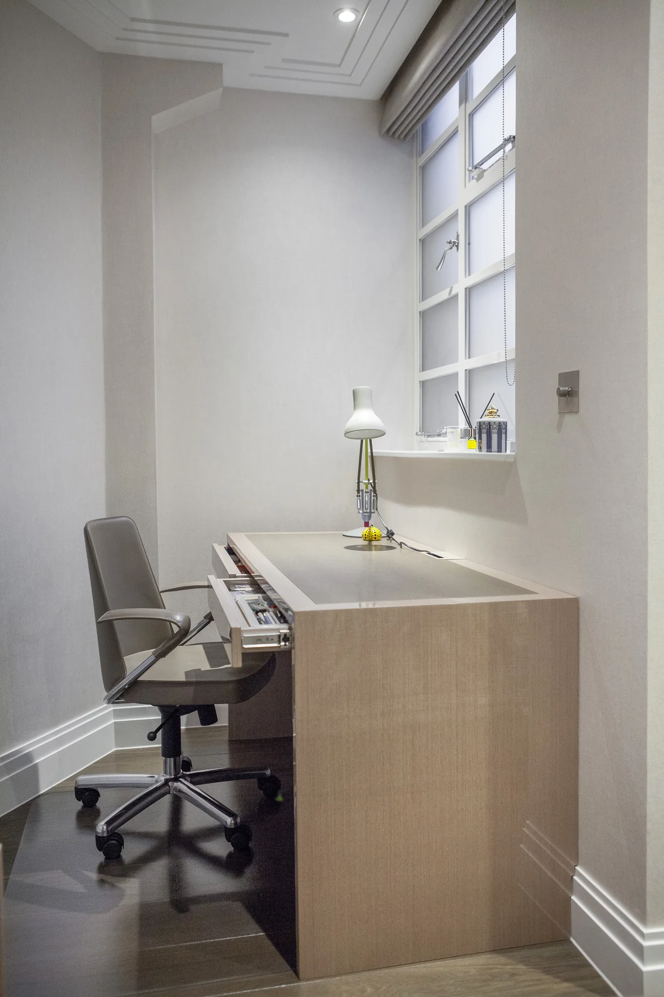 Pale fitted study desk with shallow drawers beside a window