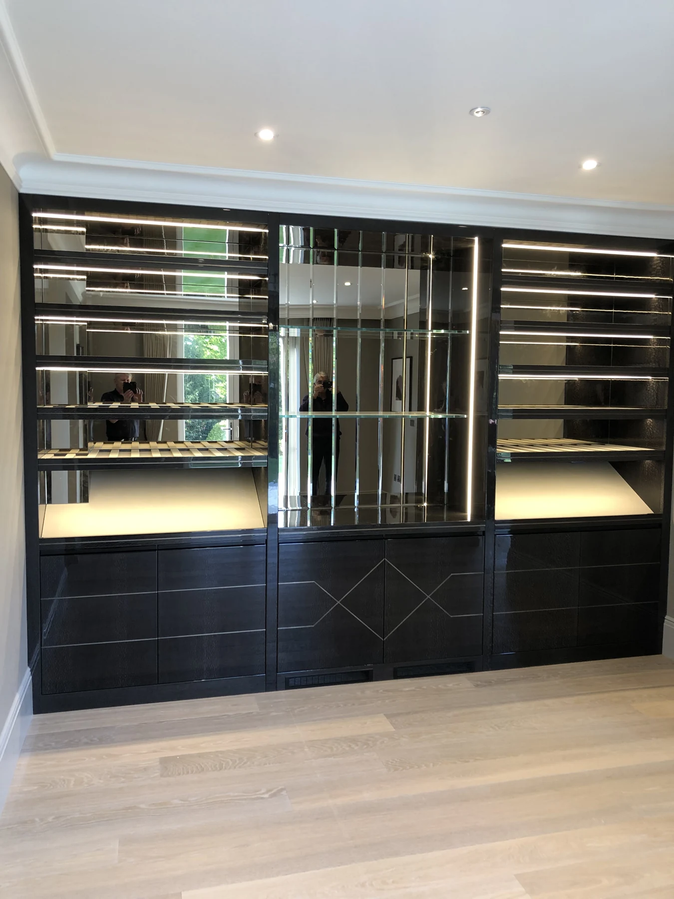 Dark mirrored drinks display with glass shelving and lower geometric door details.