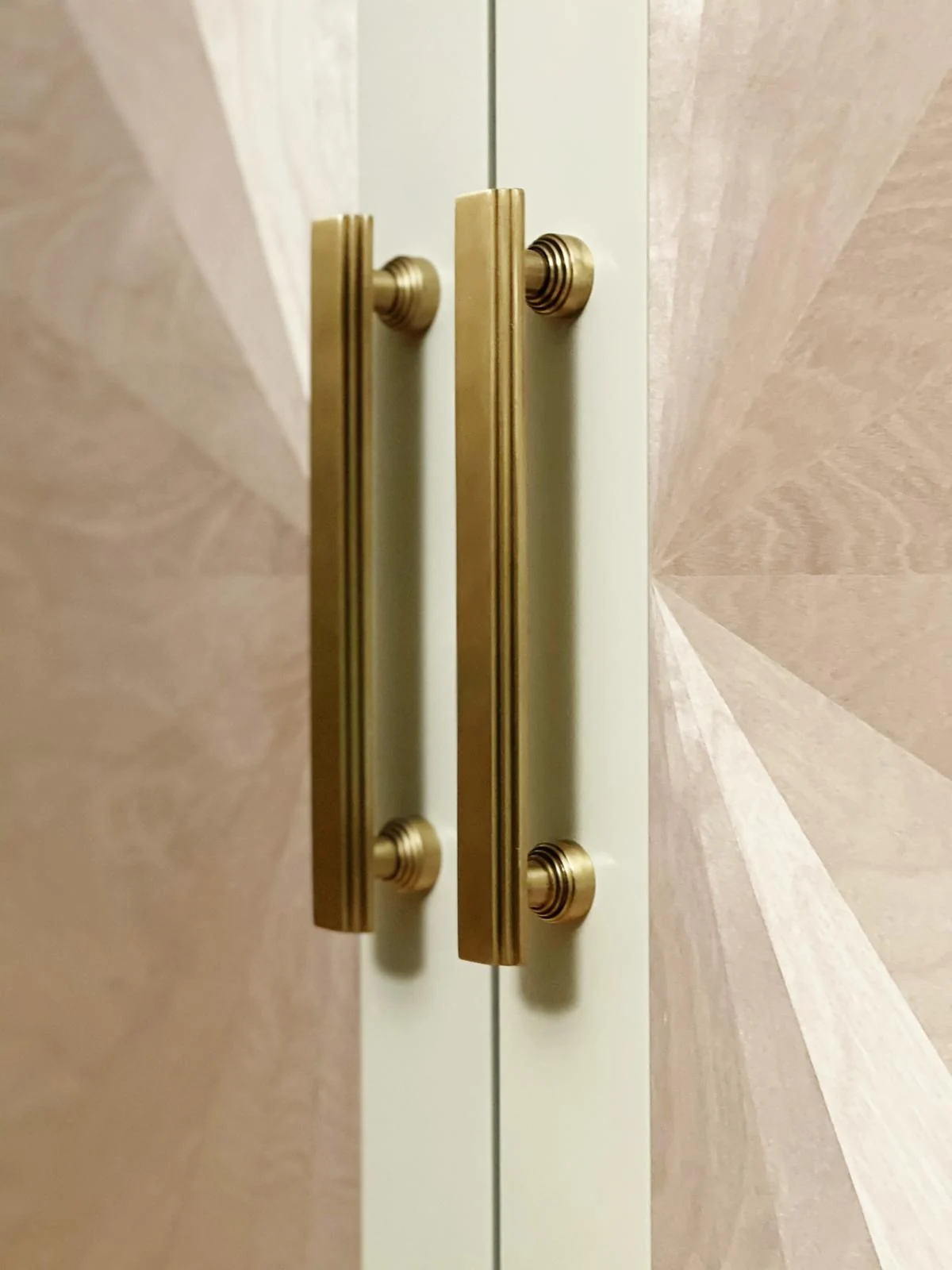 Close detail of brass-tone pull handles over the pale sunburst door pattern.