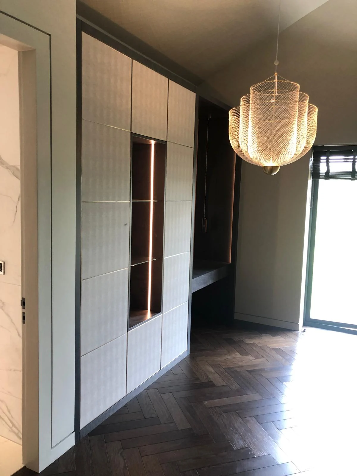 Textured fitted wardrobe with a recessed illuminated vertical compartment.