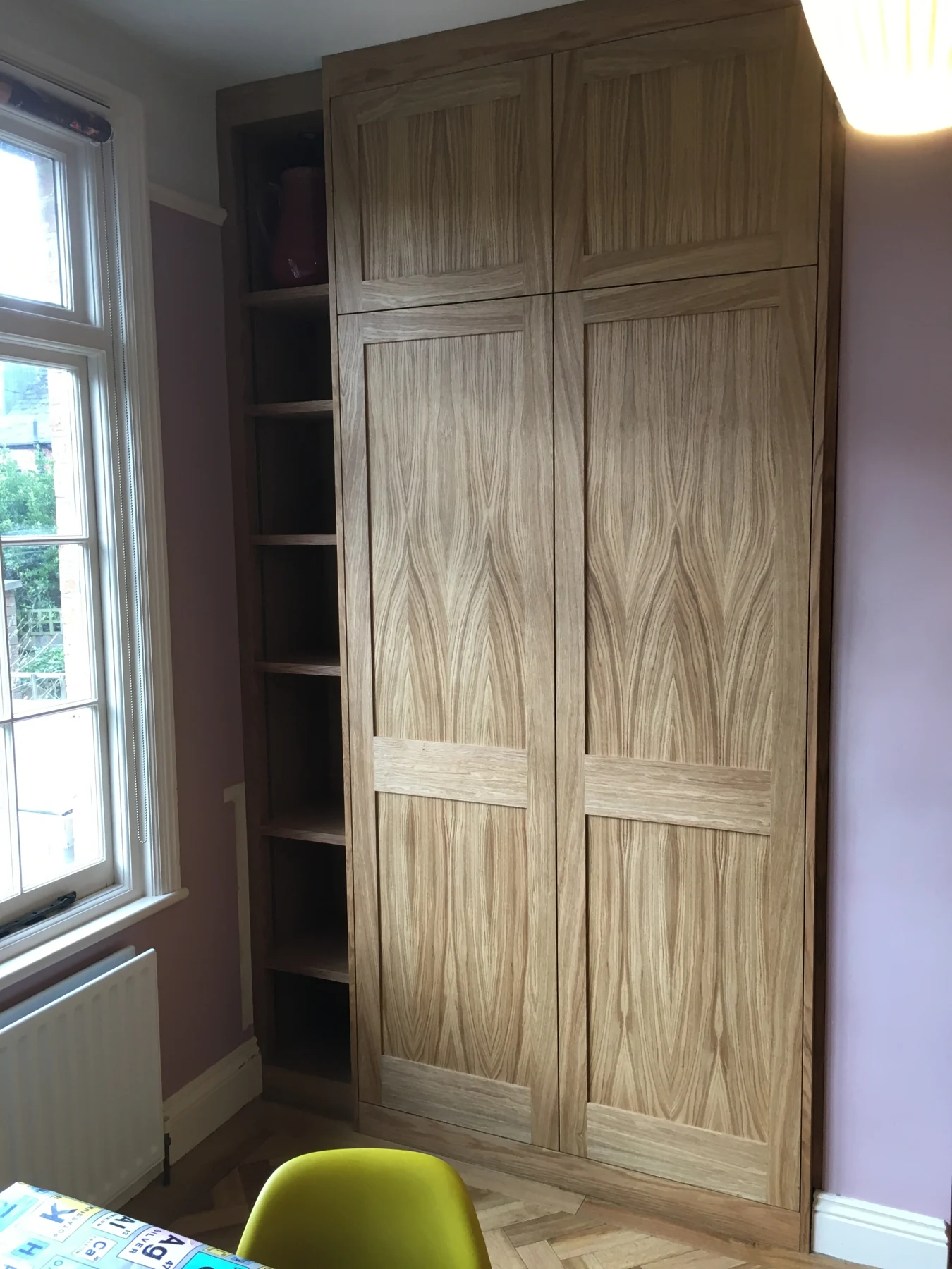Wood-grain fitted cupboard with full-height doors and adjacent shelves.